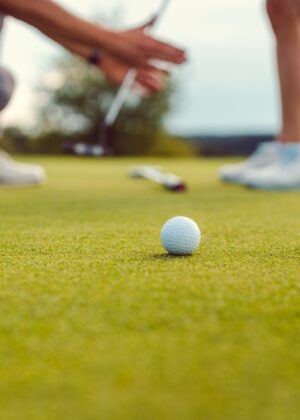 Pro on golf course teaching a woman how to put, close-up.